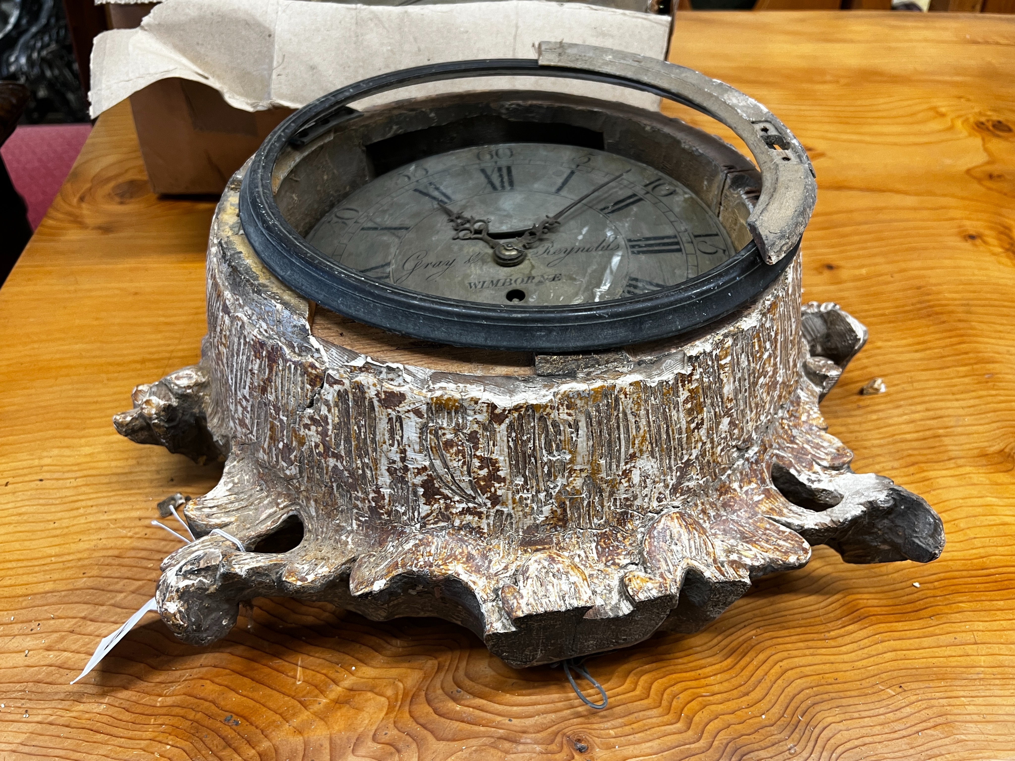 An early 19th century carved giltwood single fusee wall dial, marked Gray and Reynolds, Wimborne, dial diameter 23cm (in need of restoration), together with one other movement and three clock bezels